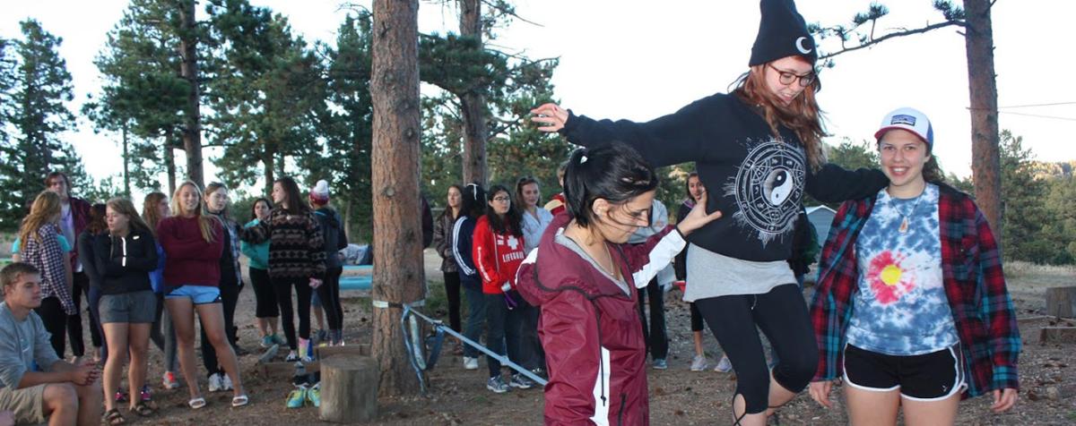 two students helping one student walk tightrope in forrest 