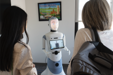 Two women, seen from behind, look at a human-like robot.