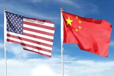 The American and Chinese flags fly on flagpoles side by side against a blue sky.