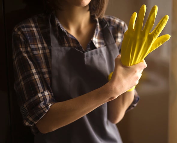 A woman holds her own hand that is inside a yellow rubber glove.