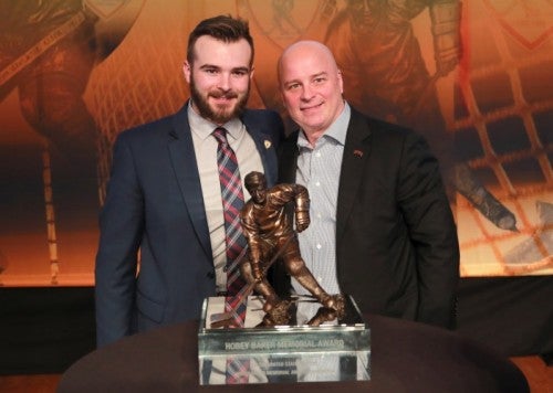 Will Butcher and Coach Jim Montgomery pose together with the Hobey Baker Award.