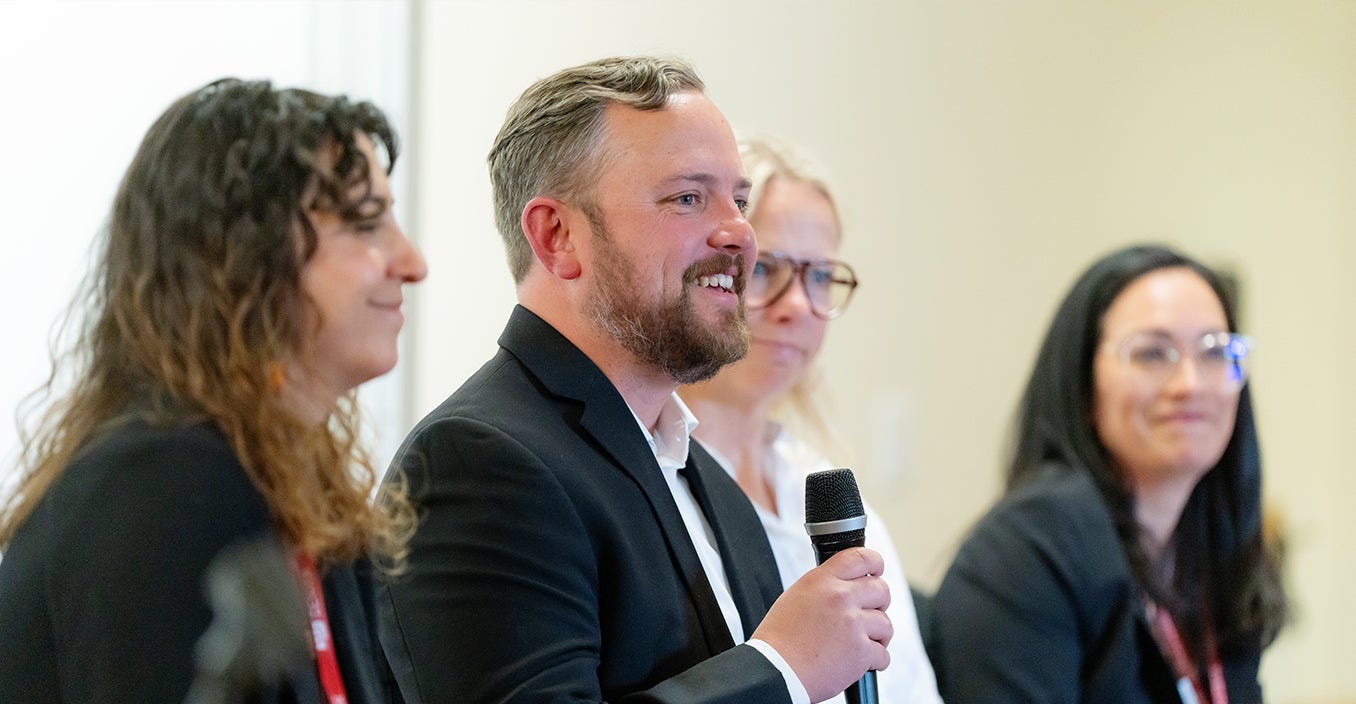 a person is speaking with a mic, the other three people are smiling