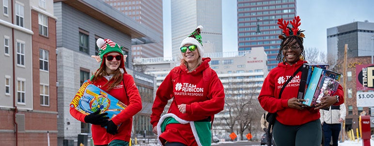 three students walking, holding gifts, at Ruck for a Claus event
