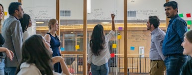 a student is writing on glass wall and a group of students are looking at her writing
