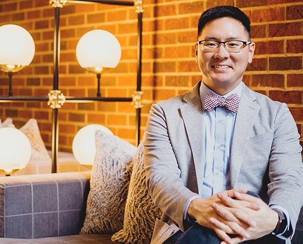 Sam Kim wearing blazer sitting with hands clasped 