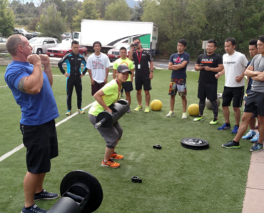 coach lifting weights with a group of athletes on a field