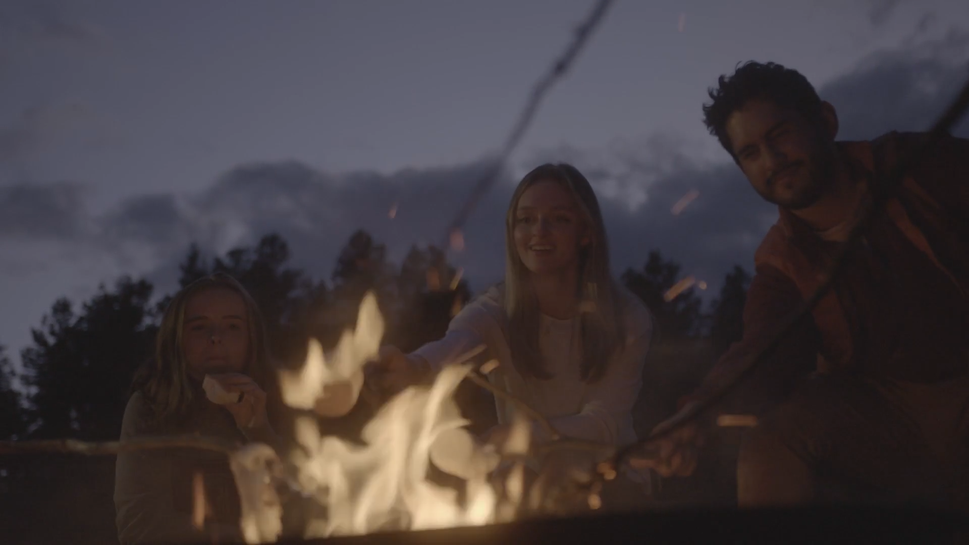 three students gathered around campfire