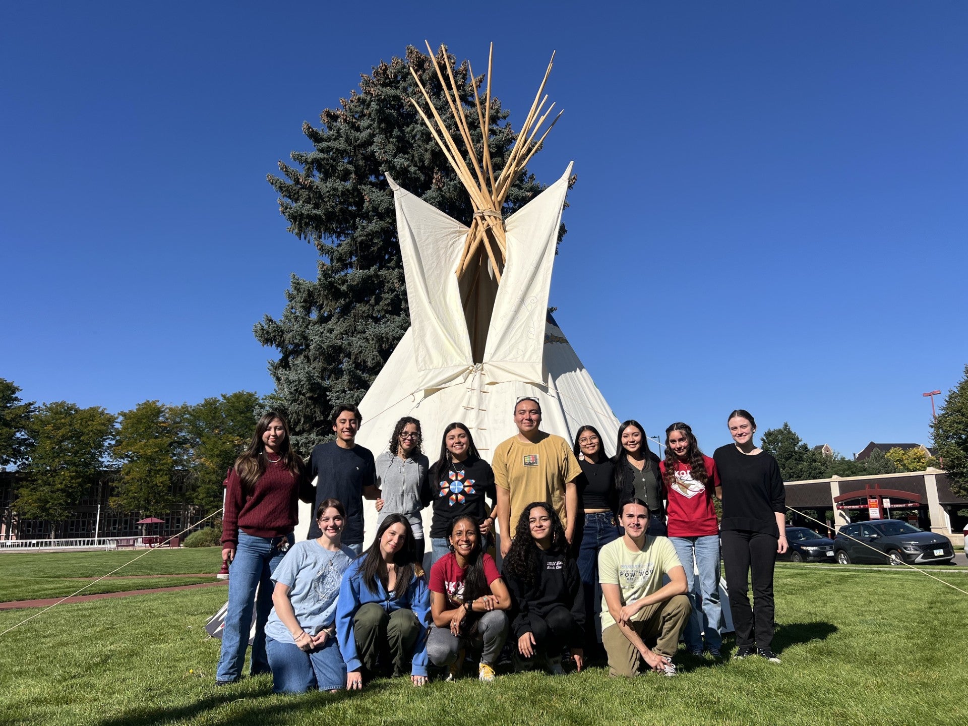 A group of students with the Native Student Alliance pose for a group photo by a canvas tipi.