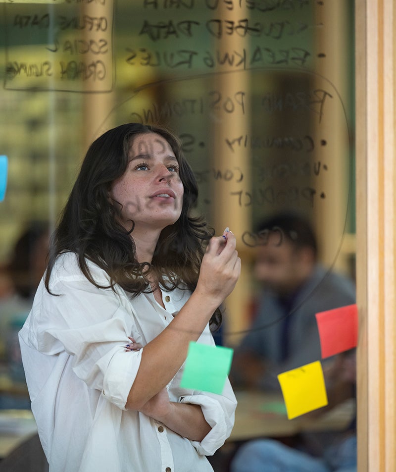 a student looking at sticky notes and writing on a glass wall