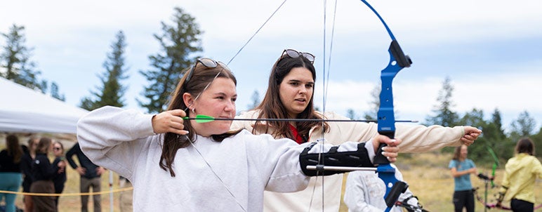a student is teaching another student archery