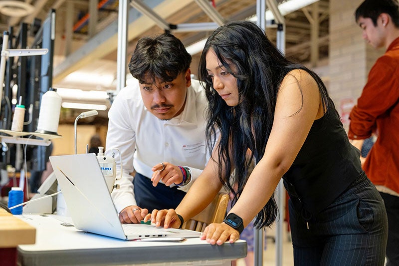 two students look at a laptop at senior design symposium
