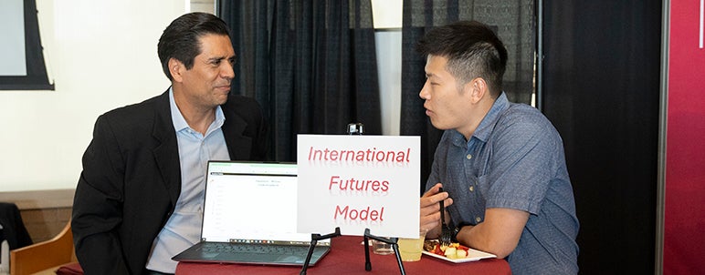 two people discussing, with a board saying "international futures model" at front