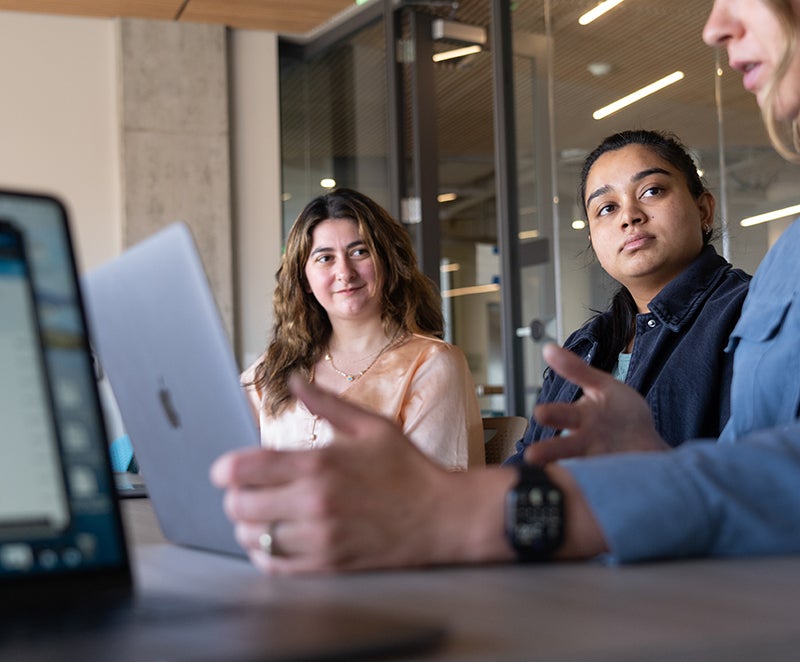 three people discussing and using their laptops