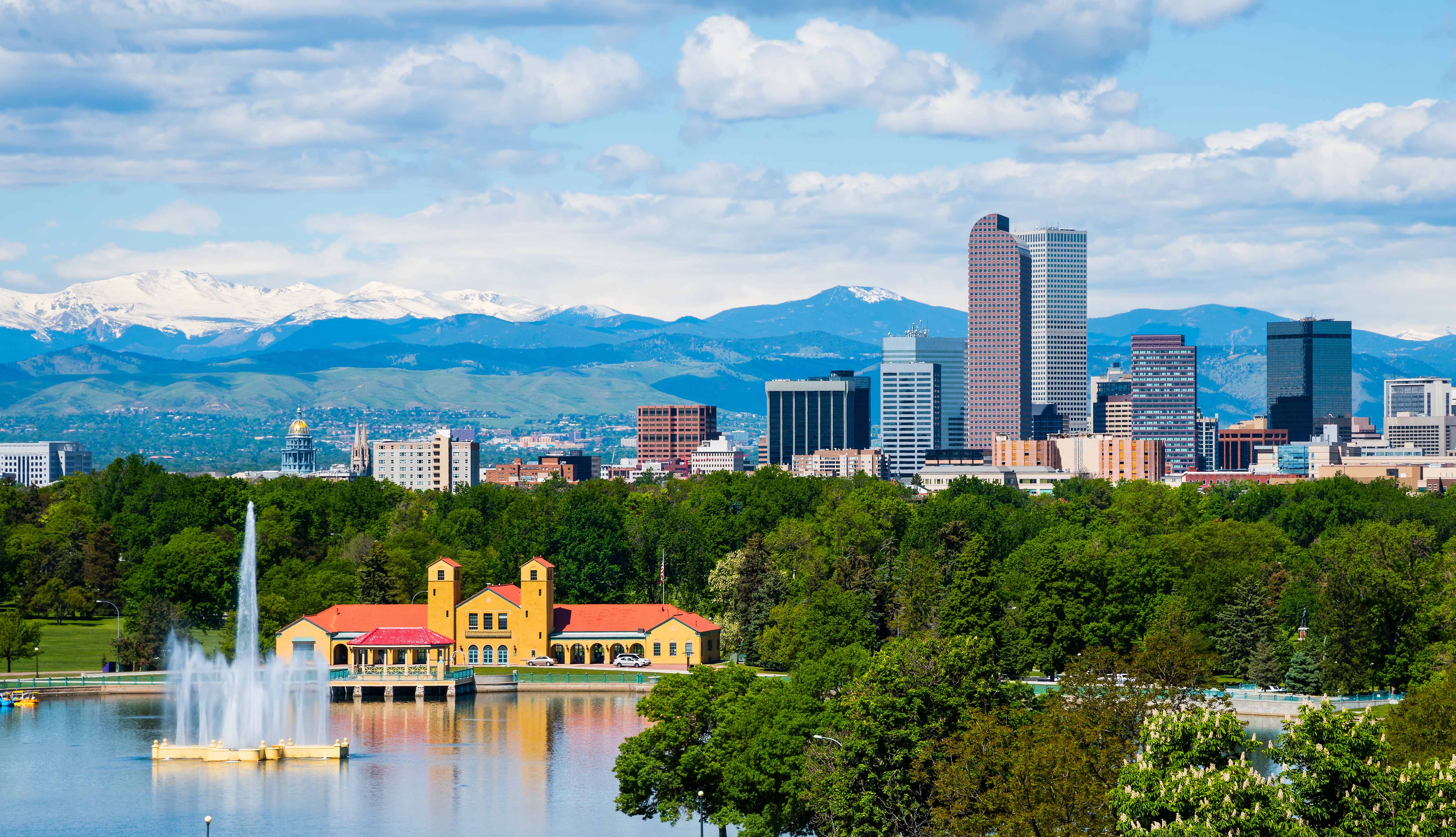 An aerial shot of Denver's City Park in front of the Denver skyline and Rocky Mountains.