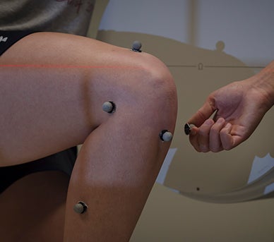 Motion tracking devices shown on a test subject's knee to test human dynamics in a lab.