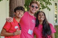 Three students in bright red t-shirts huddle for a group photo under a tree.