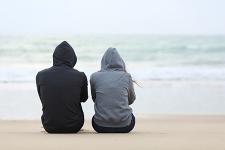 Two people sitting on a beach in hoodies