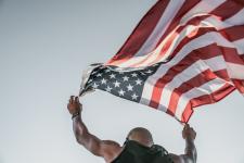 a man holding an american flag blowing in the wind