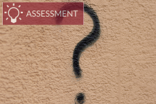 spray painted question mark on wall with text "assessment"