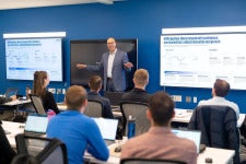 A presenter from KPMG stands next to a screen and gives a lecture to a class of DU students.