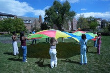 Students play with a rainbow parachute during DU's Day of Play on the Campus Green.