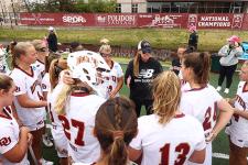 women's lacrosse team standing in a circle with coach Liza Kelly in the middle 