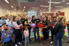Surrounded by supporters, Jessica Lopez cuts a big red ribbon on her new business, Little Legends Athletics.