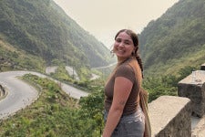 DU student Michela Schenk poses on a bridge overlooking green mountains.