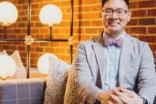 Sam Kim wearing blazer sitting with hands clasped 