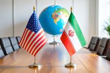 US and Iranian flags sitting on top of an empty boardroom table with an out of focus globe in background