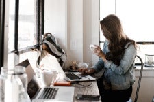 a woman works on a laptop and holds a teacup