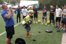 coach lifting weights with a group of athletes on a field