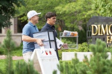 A lacrosse student at DU helps a man haul a bin on the sidewalk near the Dimond Family Residential Village.