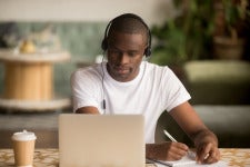male student takes notes while listening to lecture on laptop