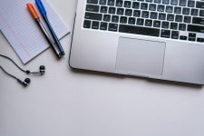 a laptop computer with pens, notepad, and earbuds
