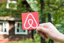 A hand holds a small piece of paper with the Airbnb logo on it.