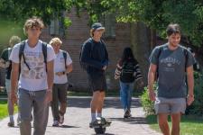 A group of young men walk and skateboard on DU's campus on a nice day.