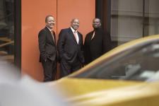 The Kenny Barron Trio stands against a wall with rushing traffic blurred in the foreground.