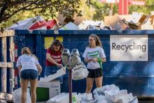 DU students throw items into a dumpster marked "recycling."