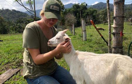 A study abroad student petting a goat in a green field