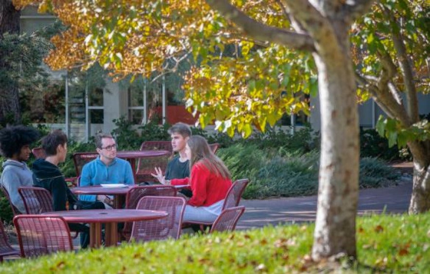 a group meets outside on a picnic table on campus
