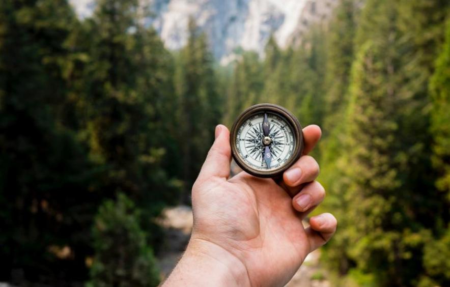 compass with hand and mountains