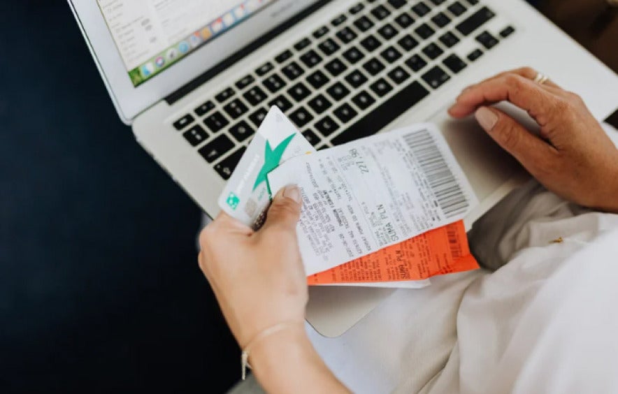 person working on a laptop with three receipts in their left hand near the keyboard