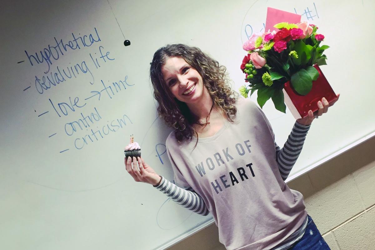 A woman standing in front of a whiteboard with flowers and a cupcake