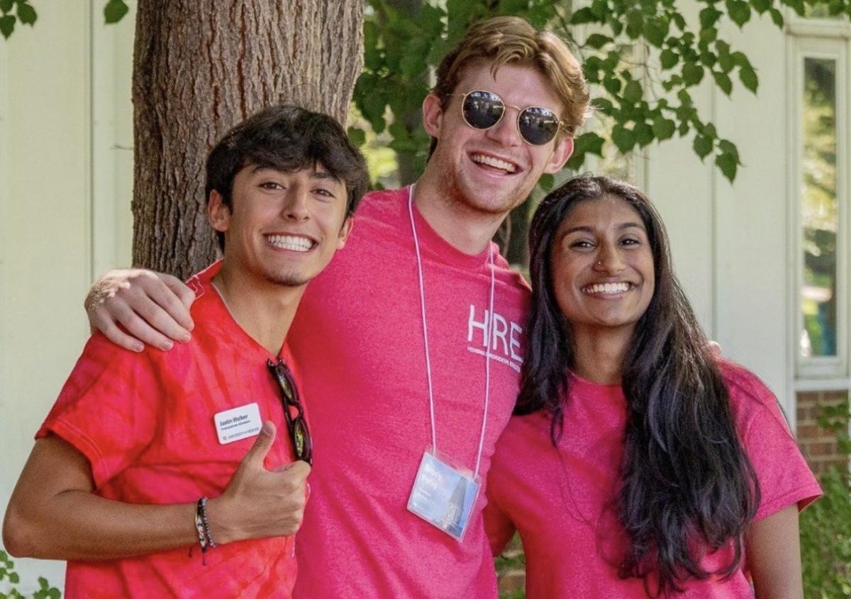 Three students in bright red t-shirts huddle for a group photo under a tree.