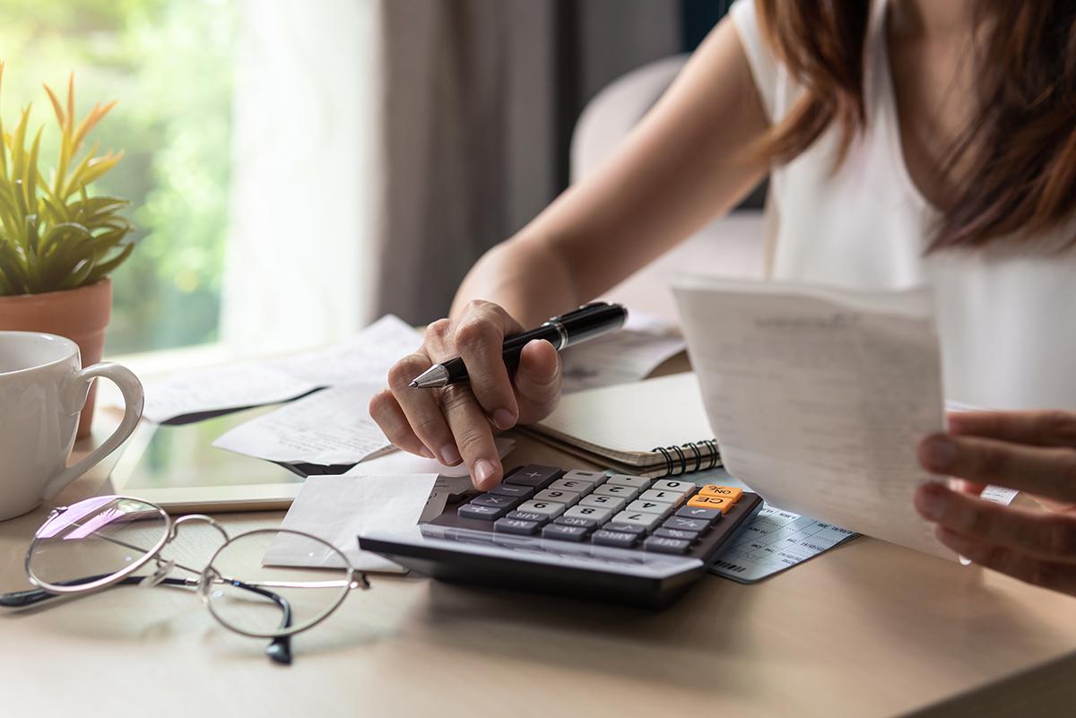 A woman holds a paper and types on a calculator
