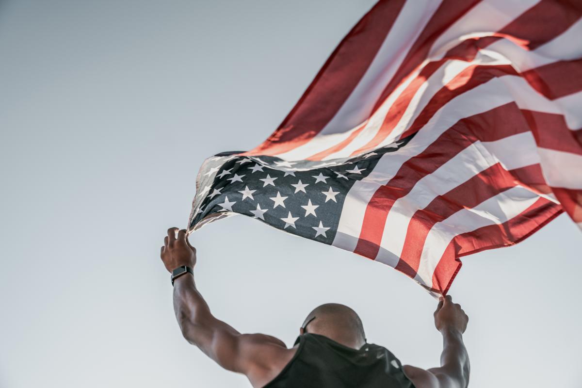 a man holding an american flag blowing in the wind