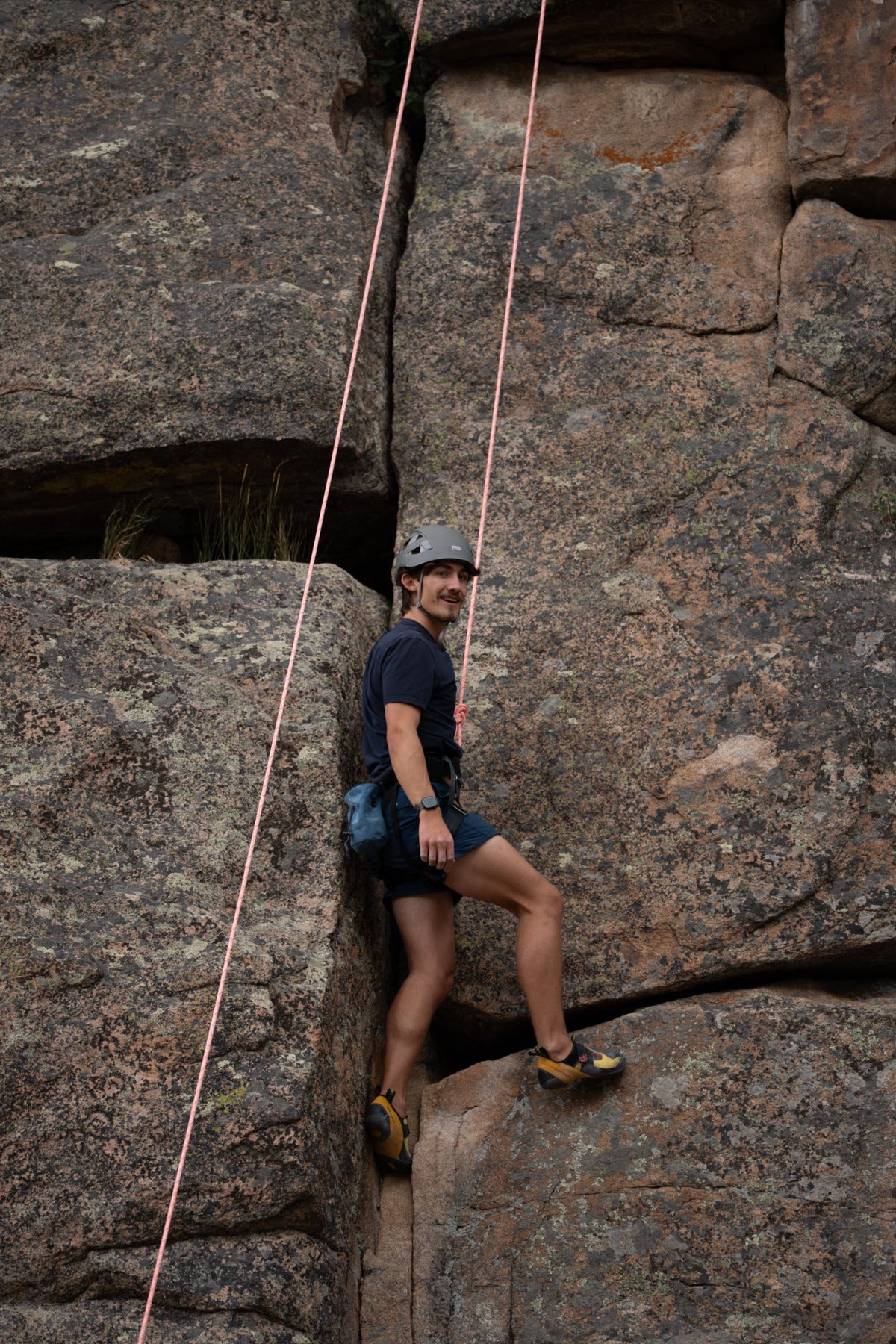 A male student grips a cliffside with the support of climbing cables.