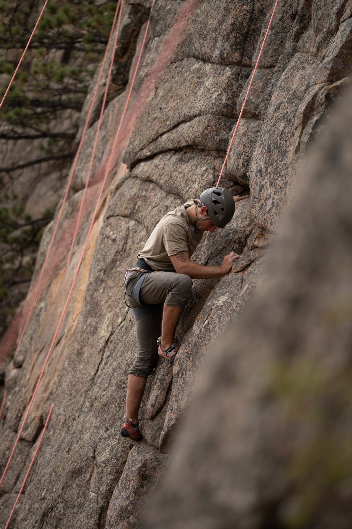 A male student grips a cliffside with the support of climbing cables.