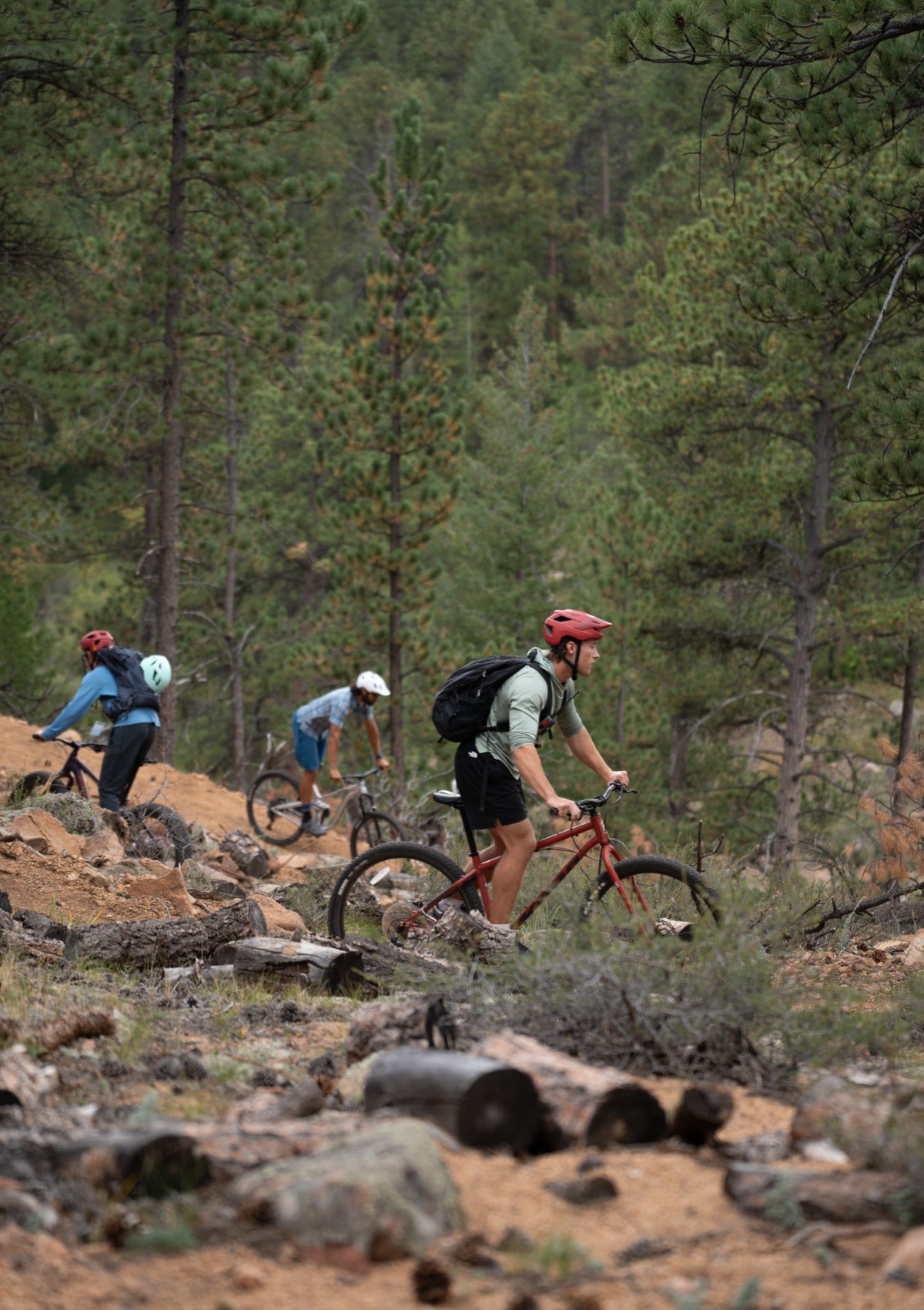Three students wearing helmets ride mountain bikes down a course at the Kennedy Mountain Campus.